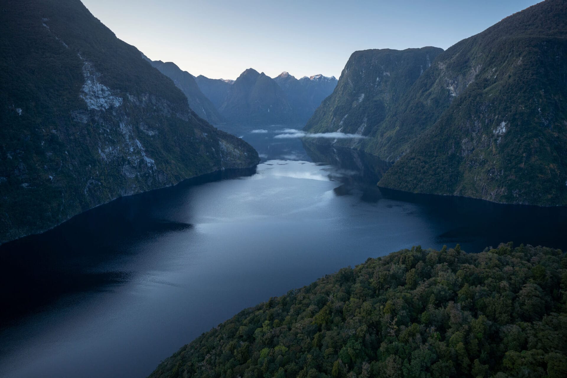 Aerial view of a serene fjord surrounded by steep forested mountains during twilight.