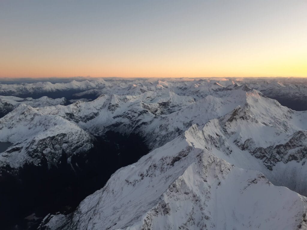 Aerial view of snow-covered mountain peaks bathed in the warm glow of a sunrise.
