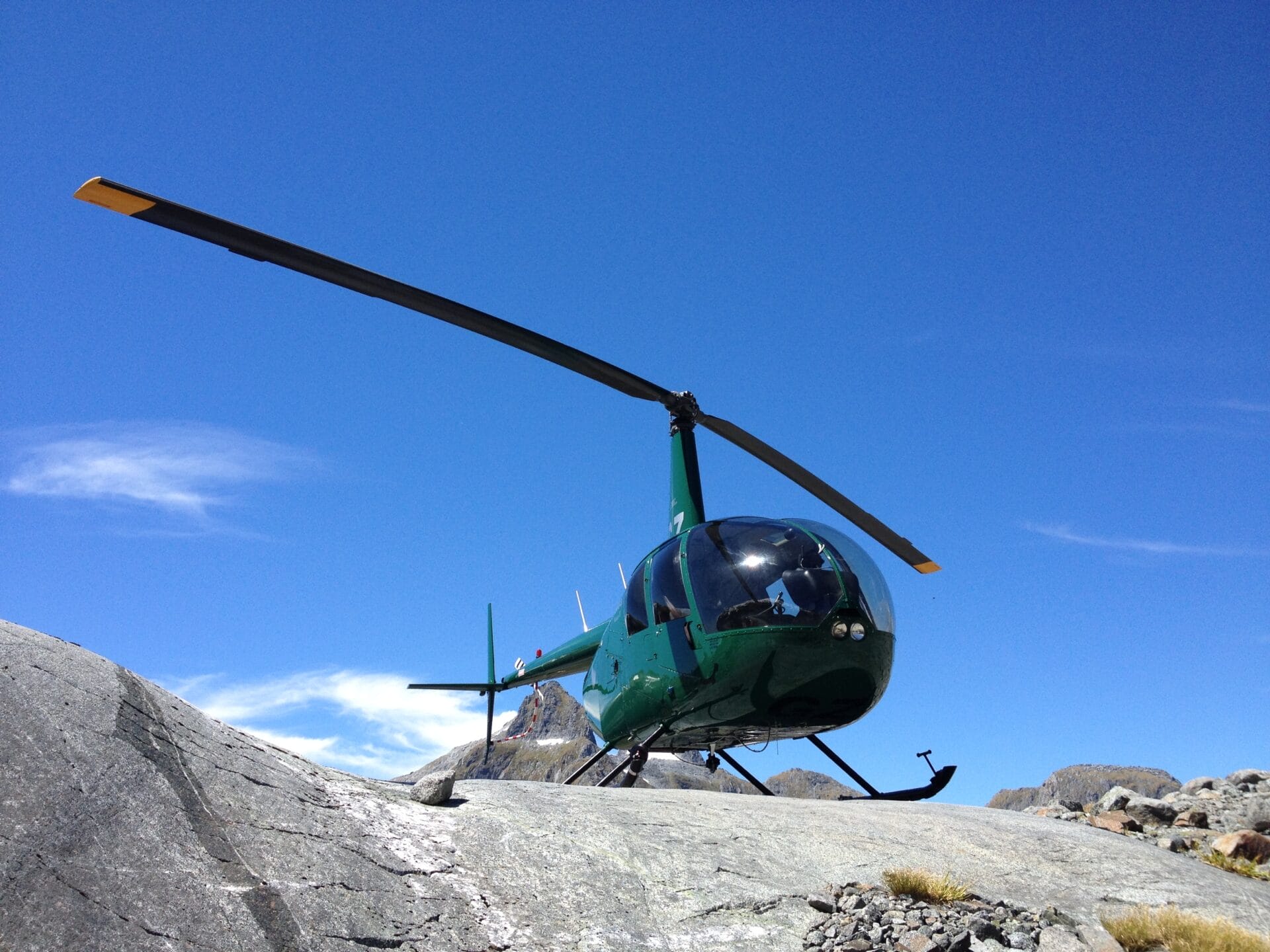 A green helicopter parked on a rocky terrain under a clear blue sky.